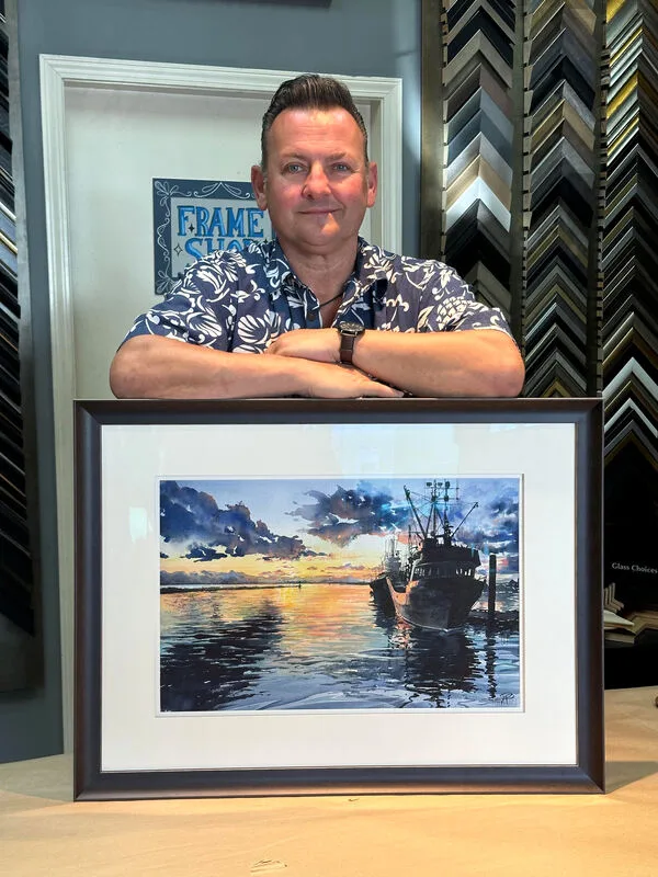 A photograph showing the artist Scott Pleydell-Pearce standing behind one of his framed watercolour paintings in Steveston, Richmond, Vancouver, British Columbia. 