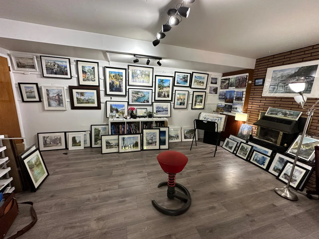 Interior gallery with lots of paintings hung on the walls. Red stool in the centre of room. 