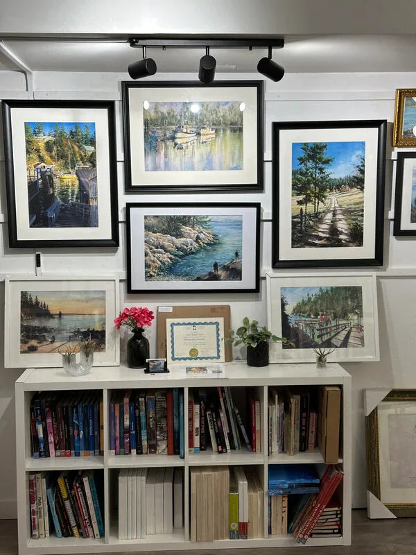 watercolour paintings in black frames on white wall above a bookcase with books.