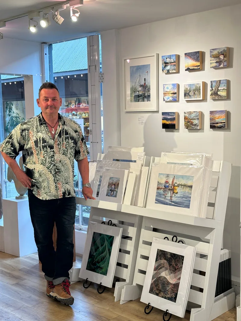 Watercolour artist Scott Pleydell-pearce standing nect to his display of painting in the UKAMA art gallery on Granville Island, Vancouver.